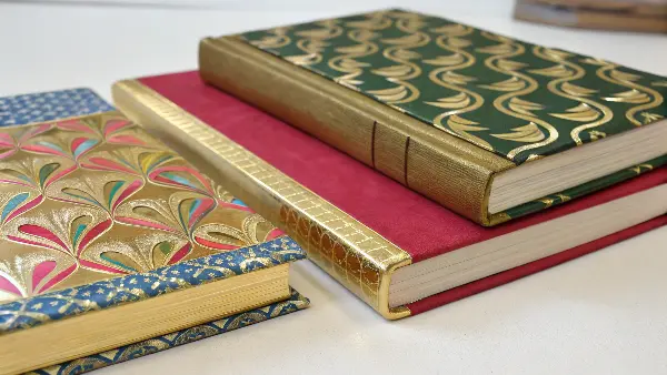 a stack of books with decorated edges showing gilding, solid color spraying, and a patterned design