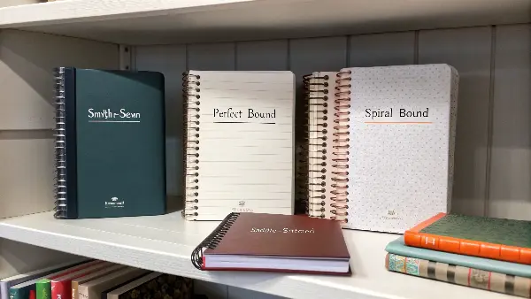 a display showing notebooks with four different binding styles: sewn, perfect, spiral, and saddle-stitched